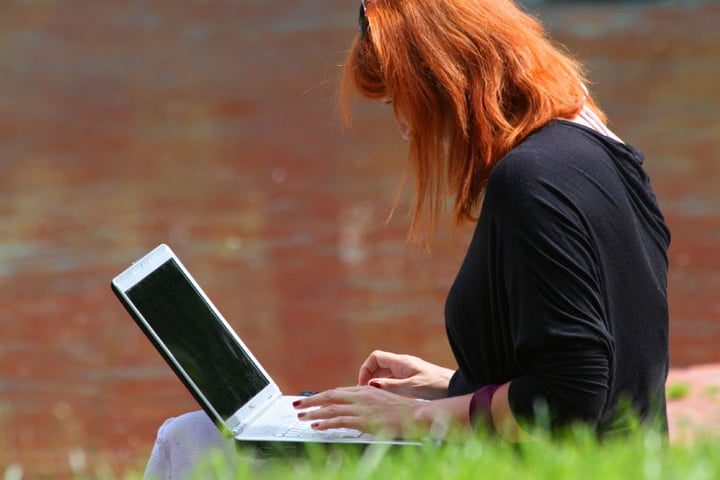 Mujer usando una portátil sobre sus piernas, en un parque
