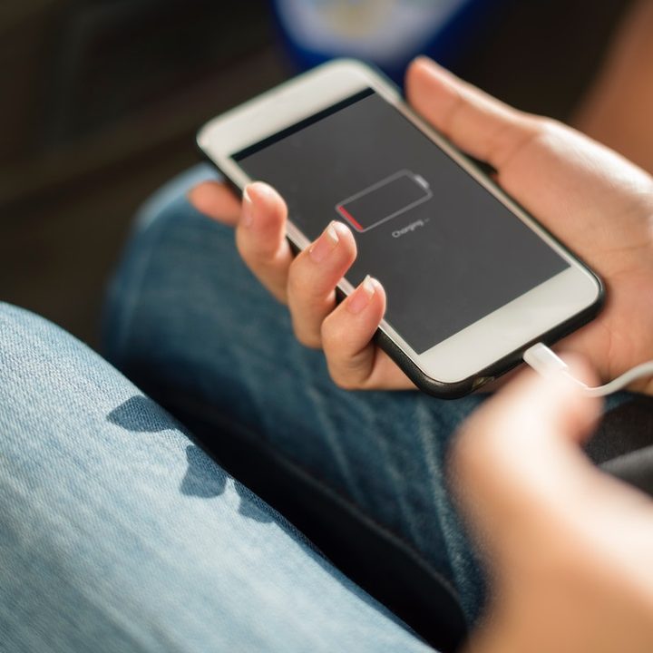 Nivel bajo de batería en un iPhone que está siendo cargado mientras una mujer con pantalones vaqueros lo sostiene en su mano.