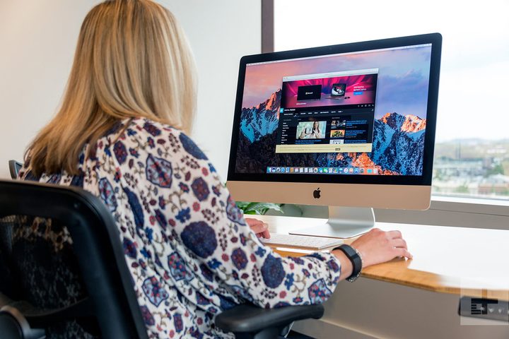Mujer vista de espaldas sentada en una silla frente a una iMac que esta sobre un escritorio buscando las mejores alternativas a iMac