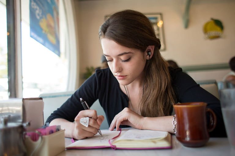 Una mujer toma apuntes mientras escucha música a través de sus audífonos inalámbricos Shure SE112, uno de los mejores productos electrónicos por menos de $100 dólares