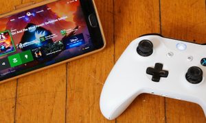 Un teléfono celular sobre una mesa junto a un control de Xbox. Te explicamos cómo conectar el teléfono a una Xbox One.