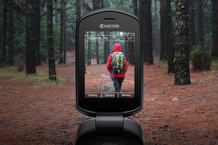 una pantalla de telefono tomando una foto de una persona con chaqueta roha y un bolso en el bosque