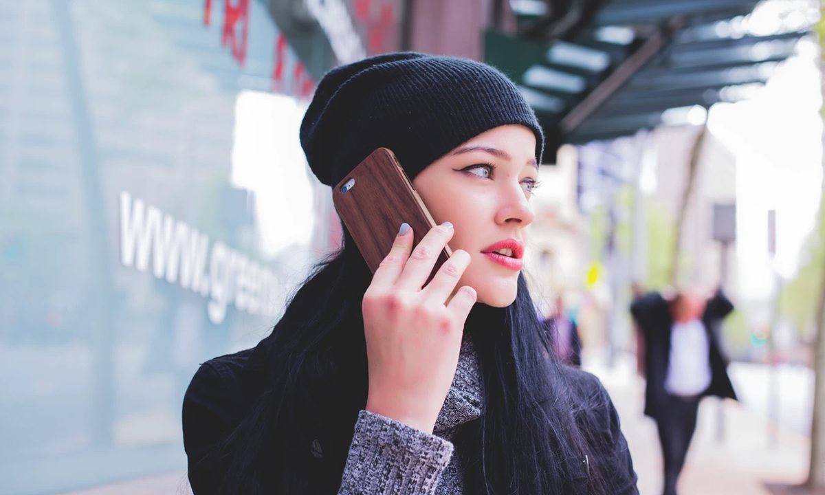 Un mujer viste un gorro mientras habla a través de un teléfono inteligente. Escogimos los mejores planes de celular en Estados Unidos