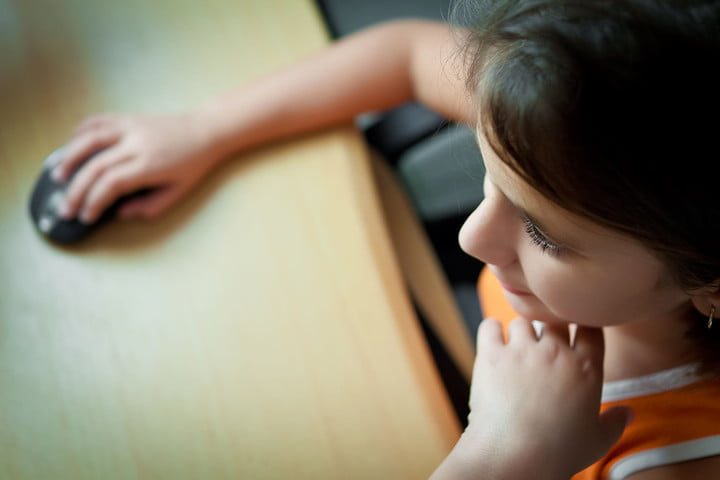 Niña vista desde arriba sentada y apoyada en un escritorio con un mouse en la mano y viendo l pantalla de una computadora la cual se ajusto para saber Cómo bloquear un sitio web