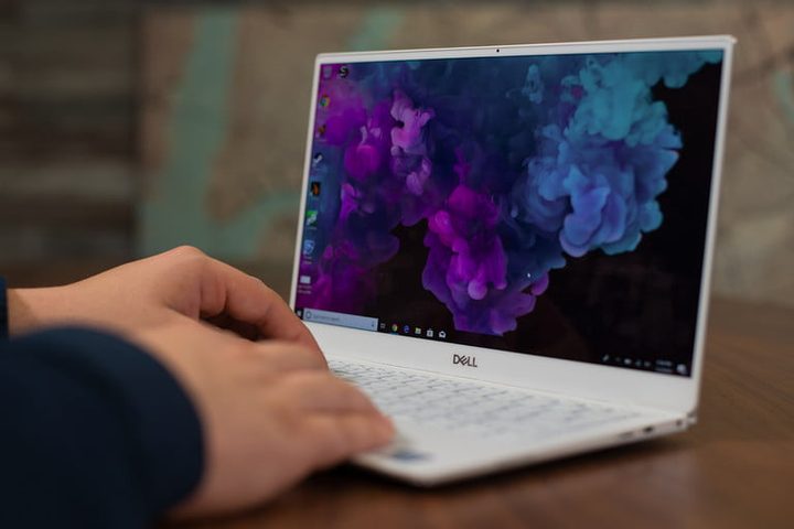 Las manos de una persona escribiendo en una Dell XPS 13 que muestra en pantalla flores azules
