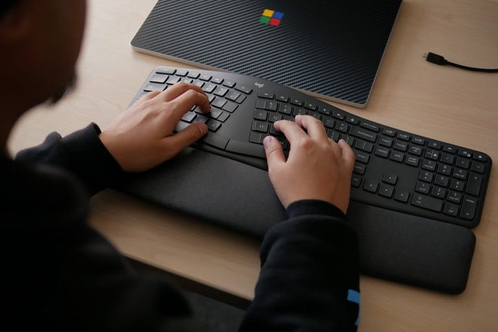 Las manos de una persona sobre el teclado Logitech Ergo K860 sobre una mesa