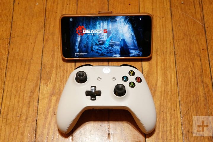 Control remoto blanco de xbox a un lado de un celular sobre una superficie de madera
