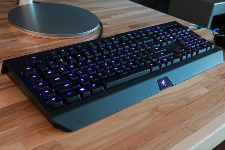 Best mechanical keyboard for gaming: Razer BlackWidow Chroma V2 sobre un escritorio de madera y junto a el un dispositivo circular plano metalico