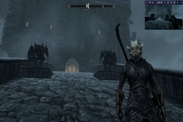 Pantalla del juego Skyrim mostrando un personaje en primer plano sobre un puente empedrado que sirve de acceso a un castillo y a los lados dos gargolas