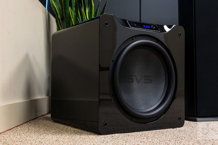 Un subwoofer negro en la esquina de una sala y atrás una planta