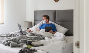 hombre con mascarilla trabajando desde su cama