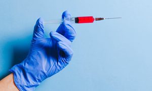 La imagen muestra una mano con guantes sujetando una inyección.