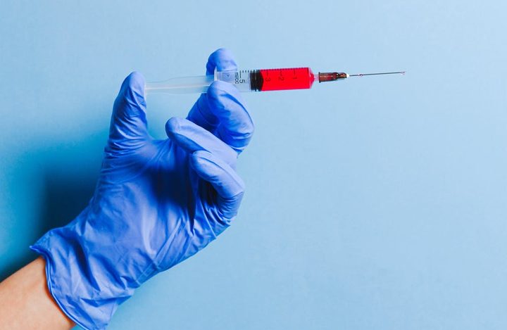 La imagen muestra una mano con guantes sujetando una inyección.
