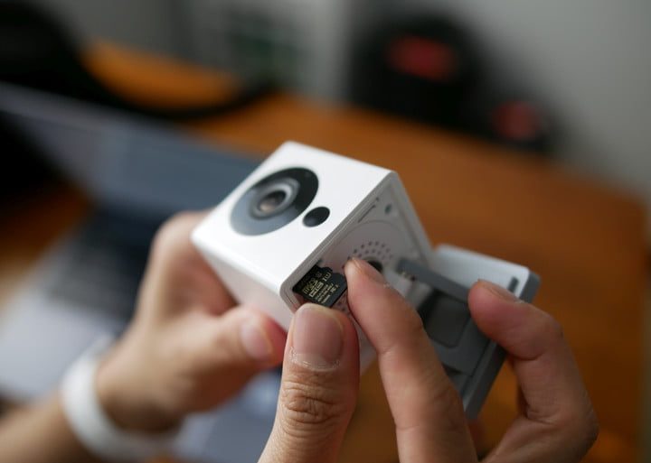Wyze Cam en las manos de una persona, insertando una microSD card para actualizar el firmware