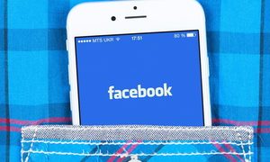 Un teléfono celular con el logo de Facebook se asoma en el bolsillo de una camisa a rayas.