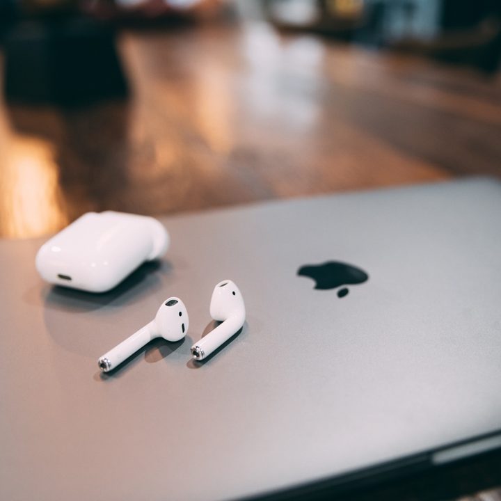 Un conjunto de audífonos Airpods junto a su estuche de carga sobre una computadora Apple
