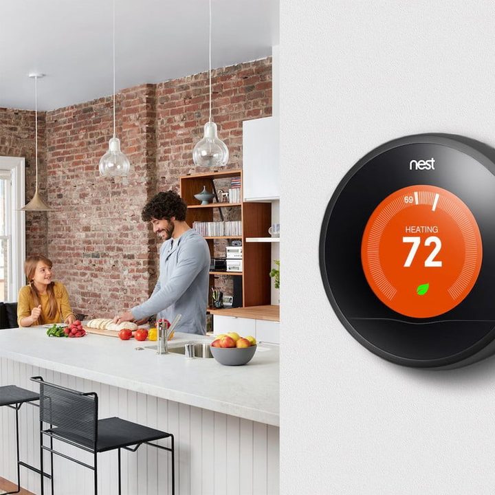 una pareja en una cocina moderna de estilo industrial y en primer plano un termostato nest colgado en la pared