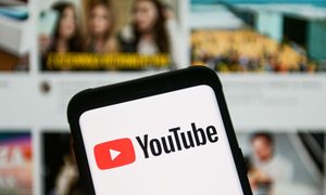 Un teléfono muestra la aplicación de YouTube con un televisor en el fondo