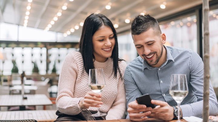 pareja tomando una copa en un bar mientras miran el móvil