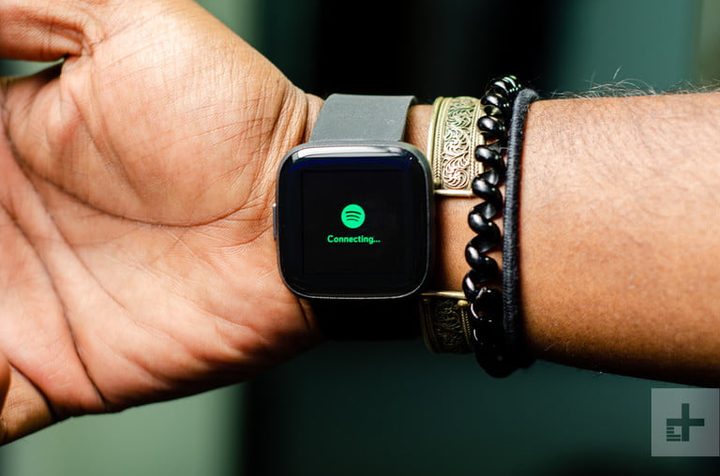 reloj fitbit versa 2 puesto en una muñeca, junto a unas pulseras, conectando con la aplicación de Spotifyy abierta