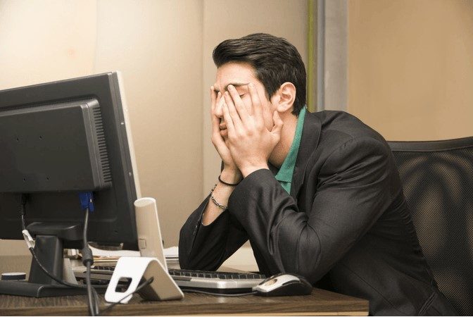 Un hombre frente a una computadora preocupado por no tener una de las mejores fuentes de alimentación de respaldo