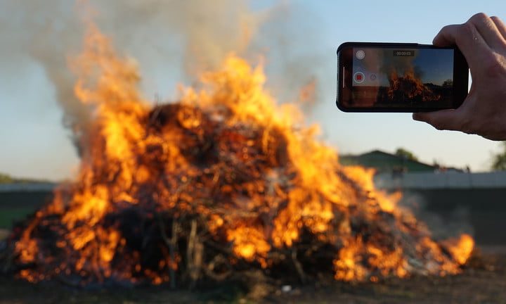 Una persona tomando foto a un montón de basura incendiándose con un celular