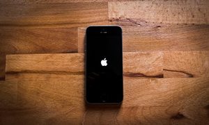 Celular sobre superficie de madera reiniciándose para revisar qué hacer cuando tu iPhone no carga la batería
