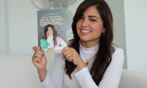 una mujer sonriendo y señalando un libro que tiene en las manos
