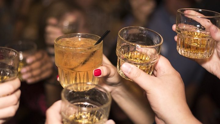 La imagen muestra varios vasos de whisky durante un brindis.