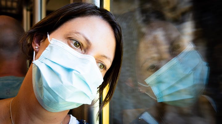 Una mujer mira desde una ventana usando una mascarilla