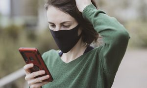 Una mujer usa una mascarilla mientras revisa su teléfono celular