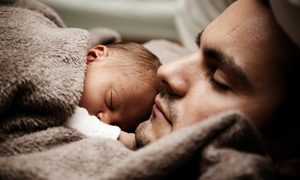 La imagen muestra a un bebé junto a su padre.