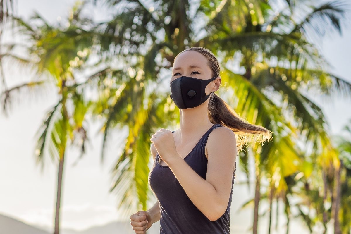 Una mujer joven con una mascarilla corre por un parque