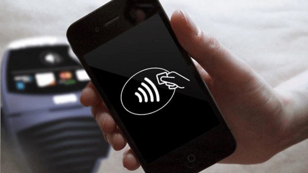 Una mano sosteniendo un celular y al fondo una terminal para aprender cómo funciona y qué es NFC