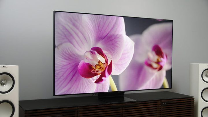 Televisor QLED sobre mueble de madera mostrando unas orquídeas para mostrar la diferencia con QD-OLED