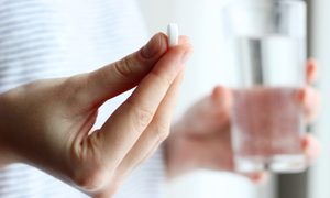 La imagen muestra una persona con un vaso de agua y una aspirina.