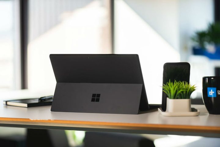 Vista trasera de Surface Pro 6 sostenida con el soporte y una planta a un lado para comparar Apple vs. Microsoft