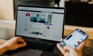 Una persona revisa su computadora con Facebook mientras sostiene un teléfono inteligente
