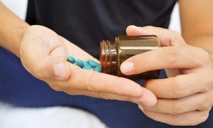 La imagen muestra a un joven manipulando un frasco de pastillas azules.