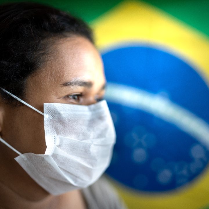 Una mujer usa una mascarilla con la bandera brasileña de fondo