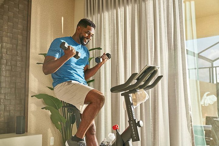 Un hombre con dos mancuernas en sus manos montado en una Echelon EX-15, una de las mejores bicicletas estáticas del mercado