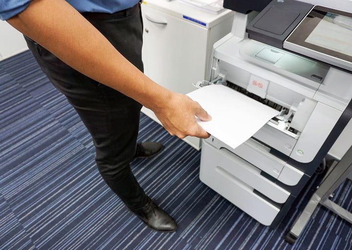 Persona de pie junto a impresora de alta demanda tomando una hoja