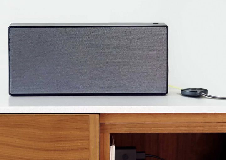 Google Chromecast en color negro sobre un escritorio junto a un altavoz