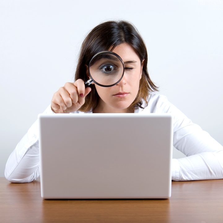 Una mujer mira con una lupa la computadora