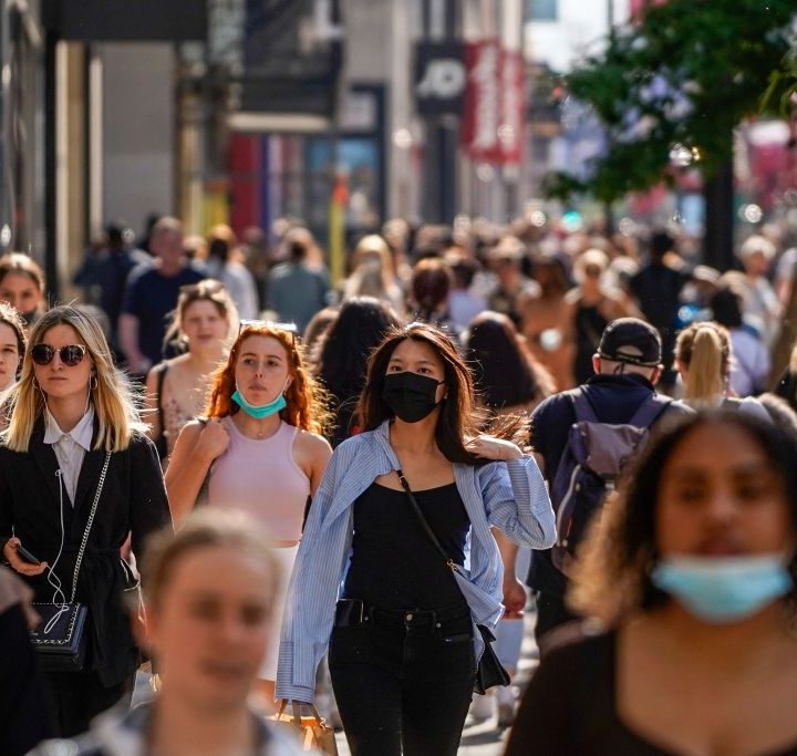 La imagen muestra a varias personas caminando con mascarillas.