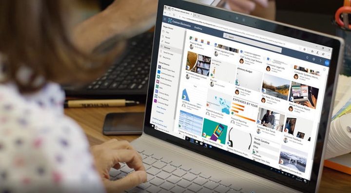 Una mujer frente a una computadora con OneDrive abierto para transferir archivos de PC a PC.