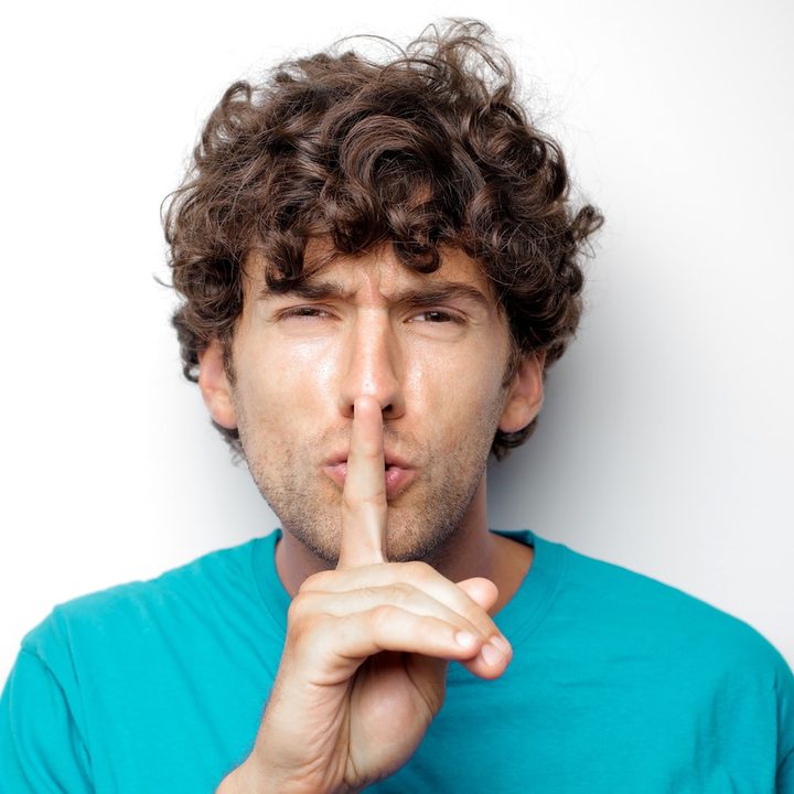 Un hombre de camisa celeste hace un gesto de silencio