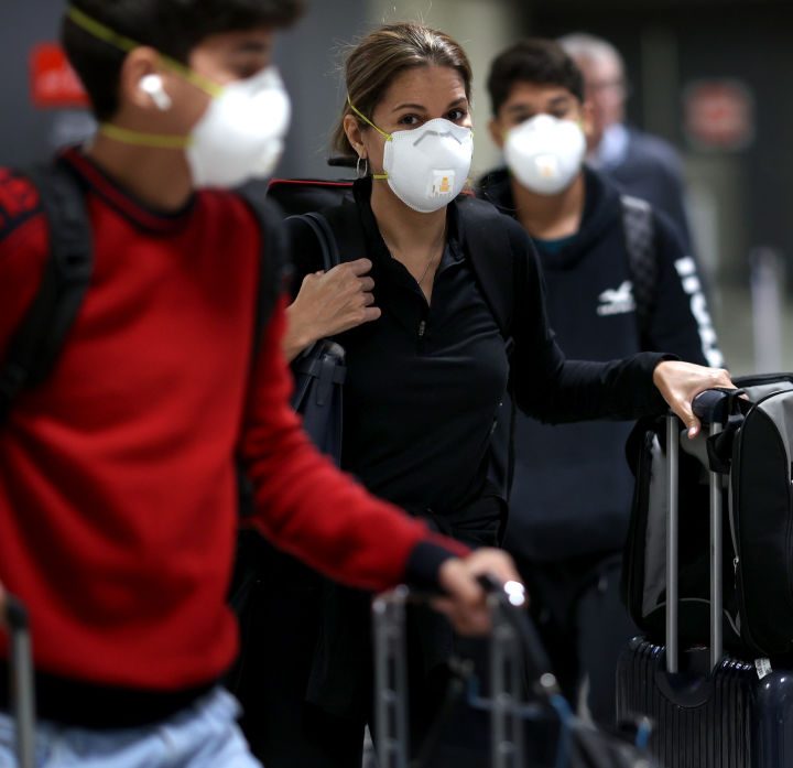 La imagen muestra a un grupo de turistas llegando a un aeropuerto en Virginia usando mascarillas.