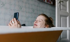 La imagen muestra a una mujer en la bañera mirando su teléfono celular.