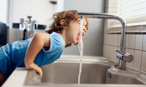La imagen muestra a un niño tomando agua desde la llave.